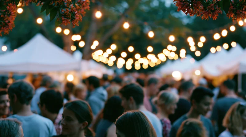 Crowd of people mingling at an outdoor evening festival under string lights and tents