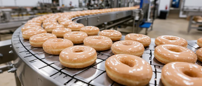 Glazed donuts moving along a curved conveyor belt in a bakery production line
