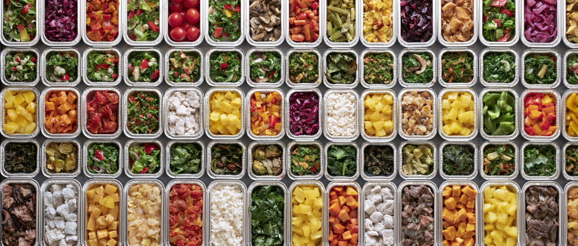 Dozens of aluminum foil takeout containers arranged in a grid, filled with colorful prepackaged meals and ingredients