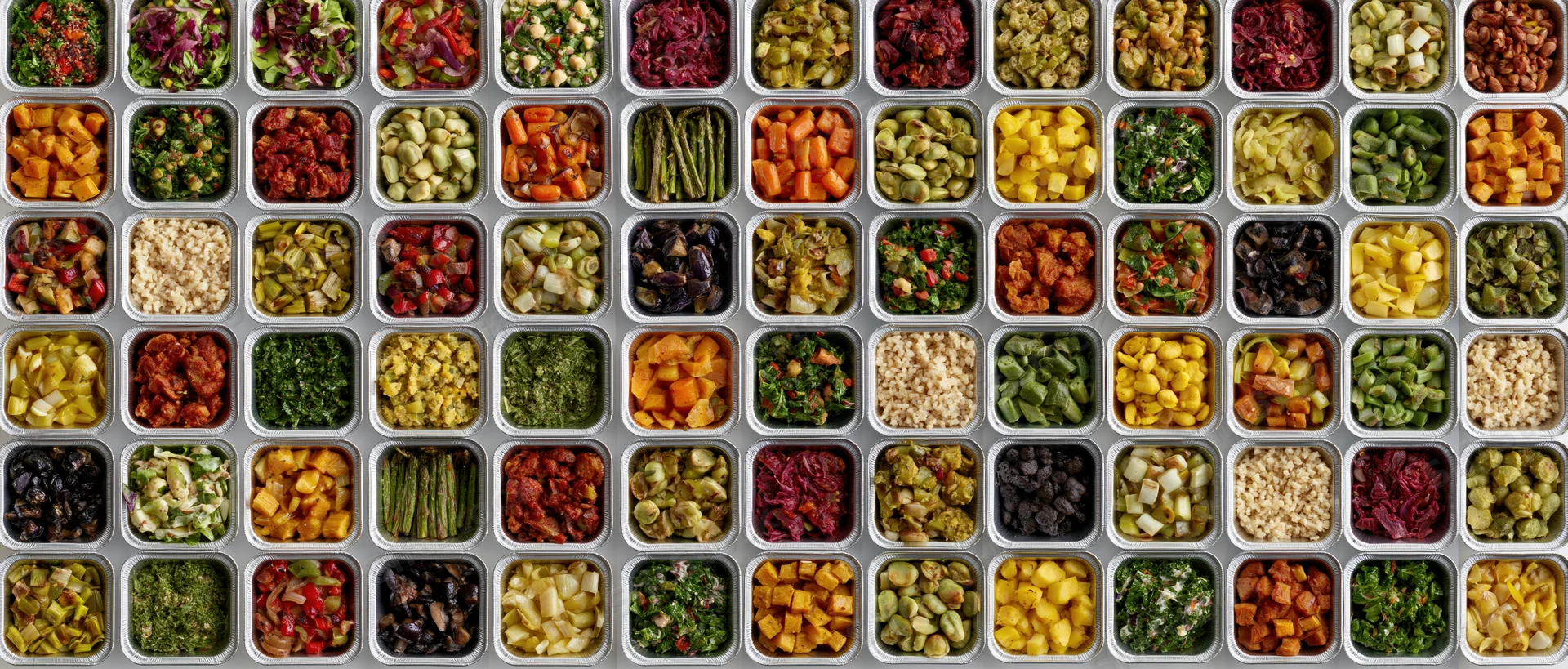 Grid of aluminum foil takeout containers filled with colorful chopped vegetables and grains, arranged in rows for meal prep