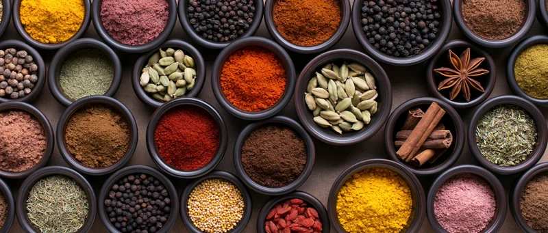 Overhead view of dark ceramic bowls filled with various whole and ground spices arranged in a grid pattern