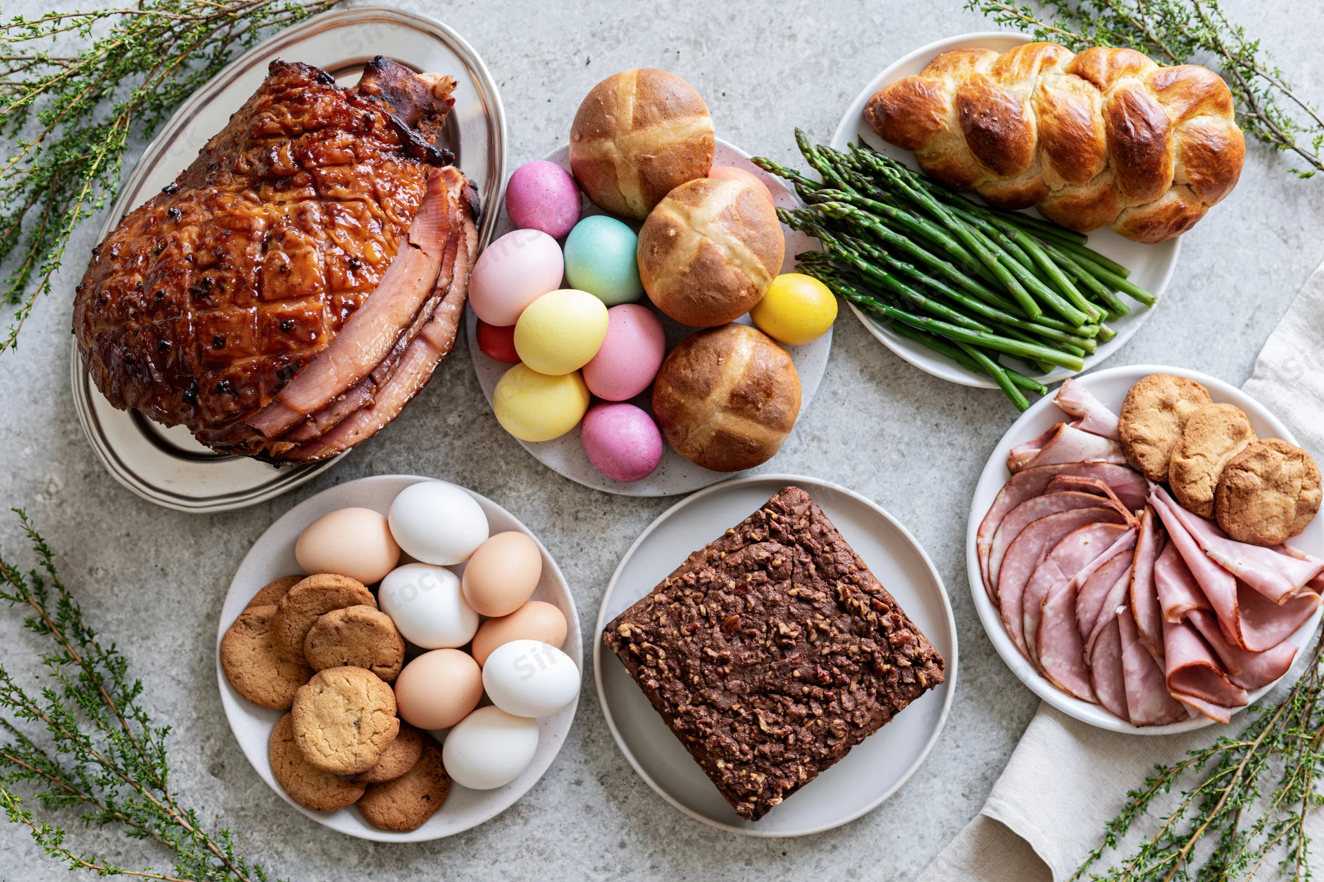 Easter holiday food spread with ham, eggs, bread, asparagus, cookies, and cake on a stone surface