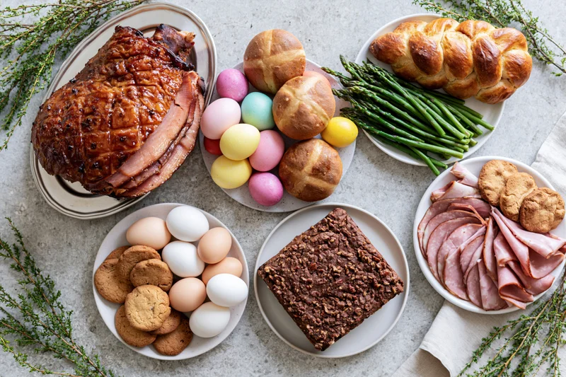 Easter holiday food spread with ham, eggs, bread, asparagus, cookies, and cake on a stone surface