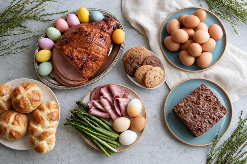 Easter holiday food spread with ham, eggs, bread and desserts arranged on a stone table