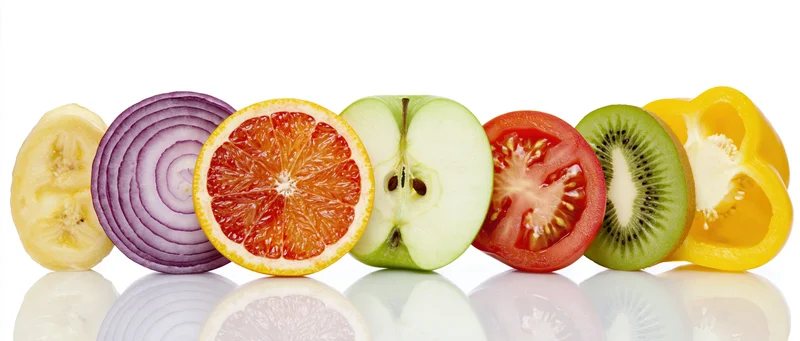 Cross-sections of fruit and vegetables arranged in a row on a reflective white surface