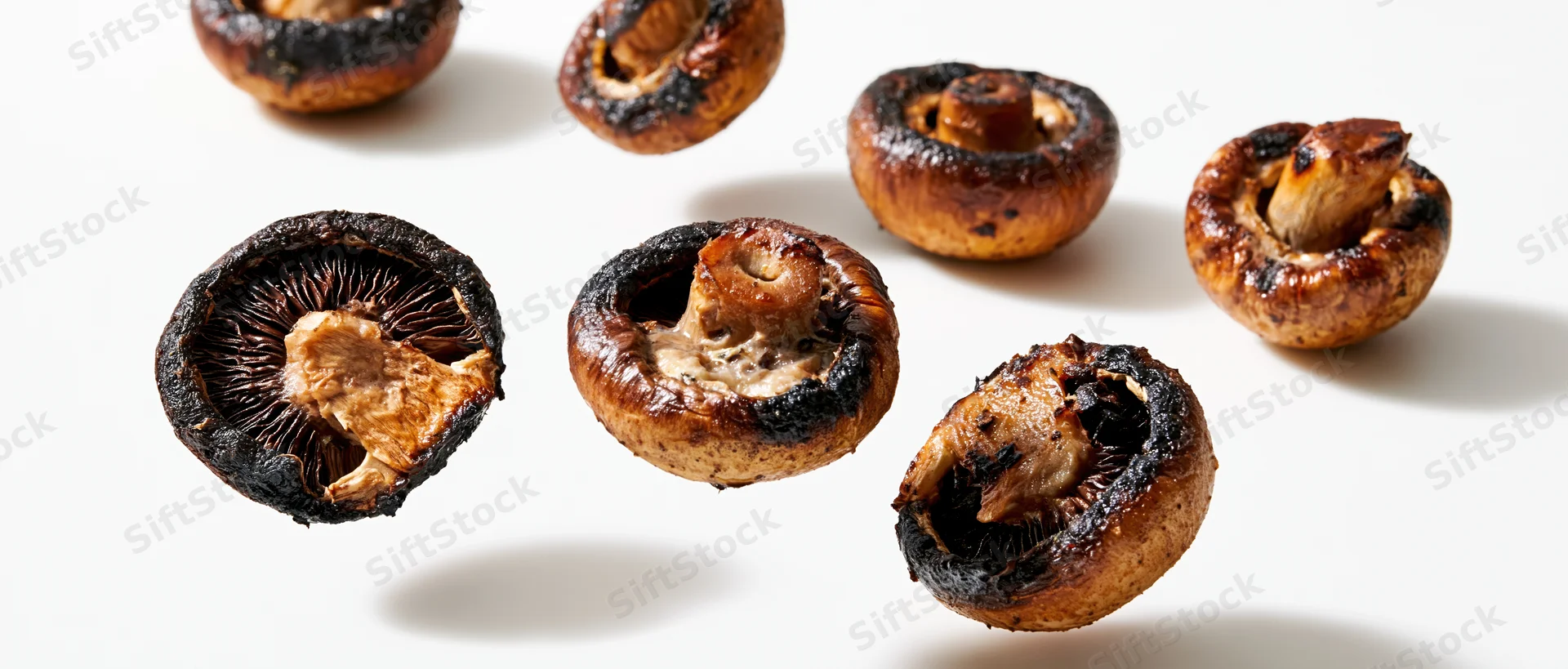 Grilled cremini mushroom halves floating midair against white background
