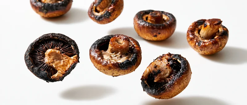 Grilled cremini mushroom halves floating midair against white background