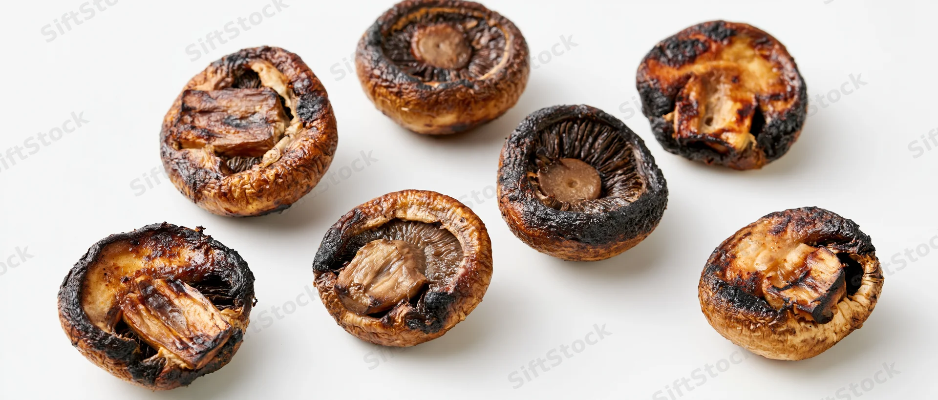 Grilled cremini mushroom halves scattered on white surface