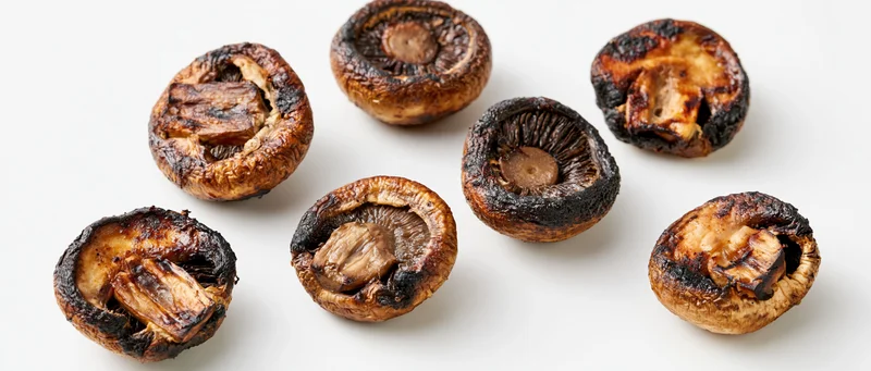 Grilled cremini mushroom halves scattered on white surface