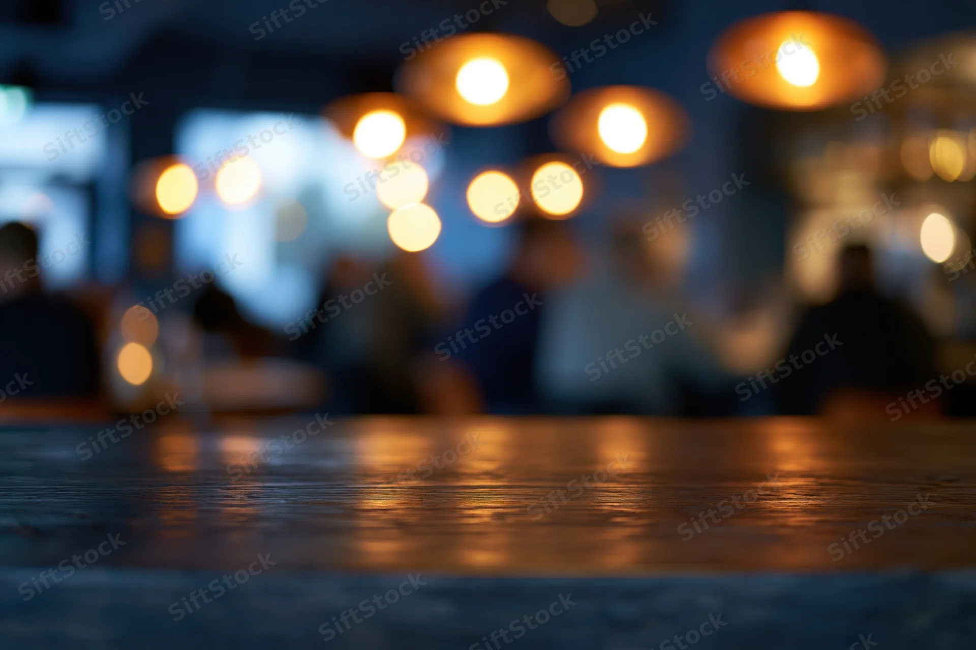 Empty dark wooden bar counter in foreground with blurred background of people and warm lights