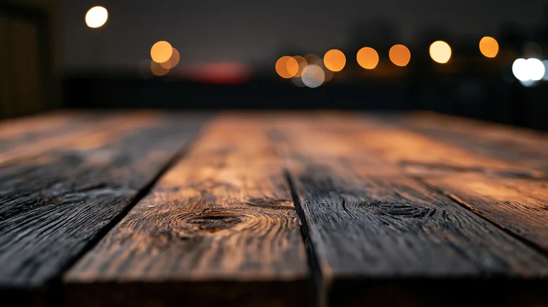 Low-angle view of empty rustic wooden tabletop with blurred lights in background