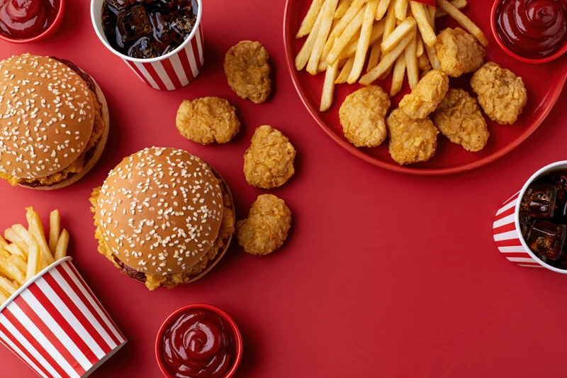 Fast food meal with burgers, fries, chicken nuggets and soda arranged on red surface