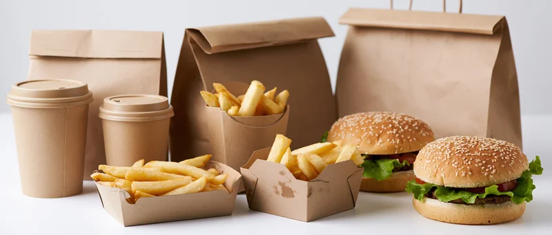 Fast food takeout items including burgers, fries, and drinks arranged on a white surface in paper packaging