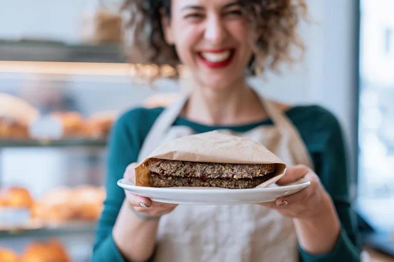 Woman in apron holding plate with wrapped sandwich in cafe