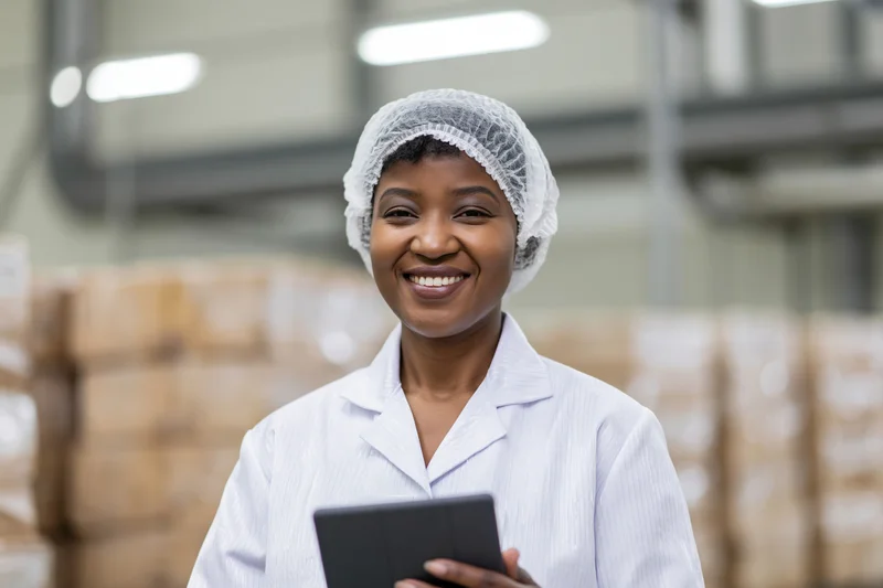 Smiling woman in lab coat holding tablet in factory warehouse