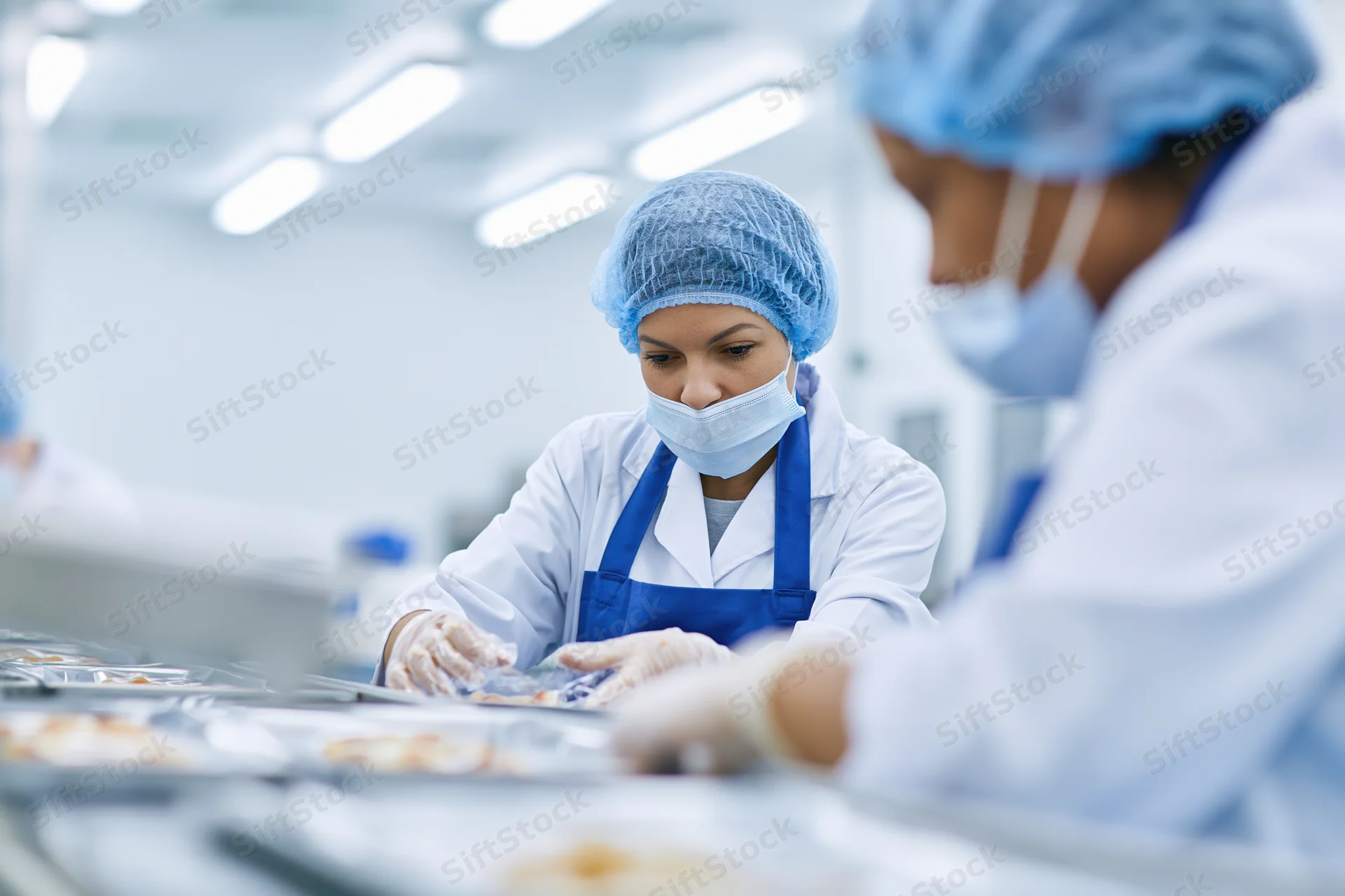 Woman in protective gear arranging food packages on a conveyor line in a cleanroom factory