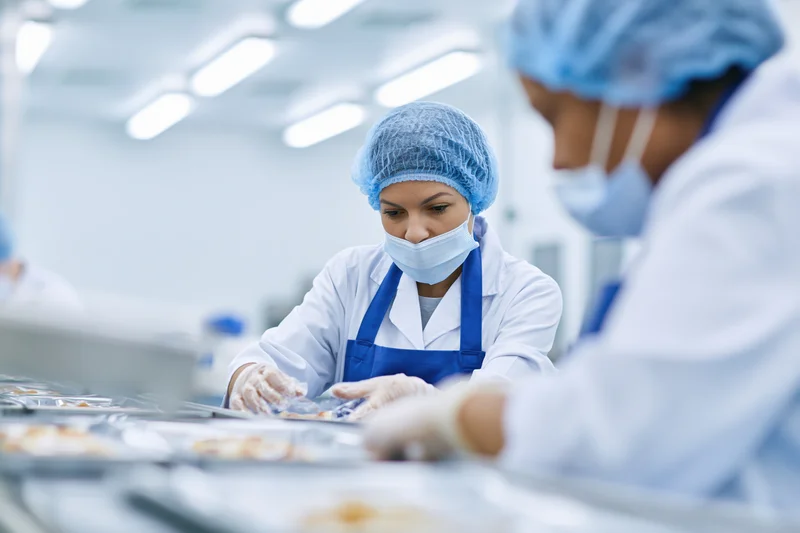 Woman in protective gear arranging food packages on a conveyor line in a cleanroom factory