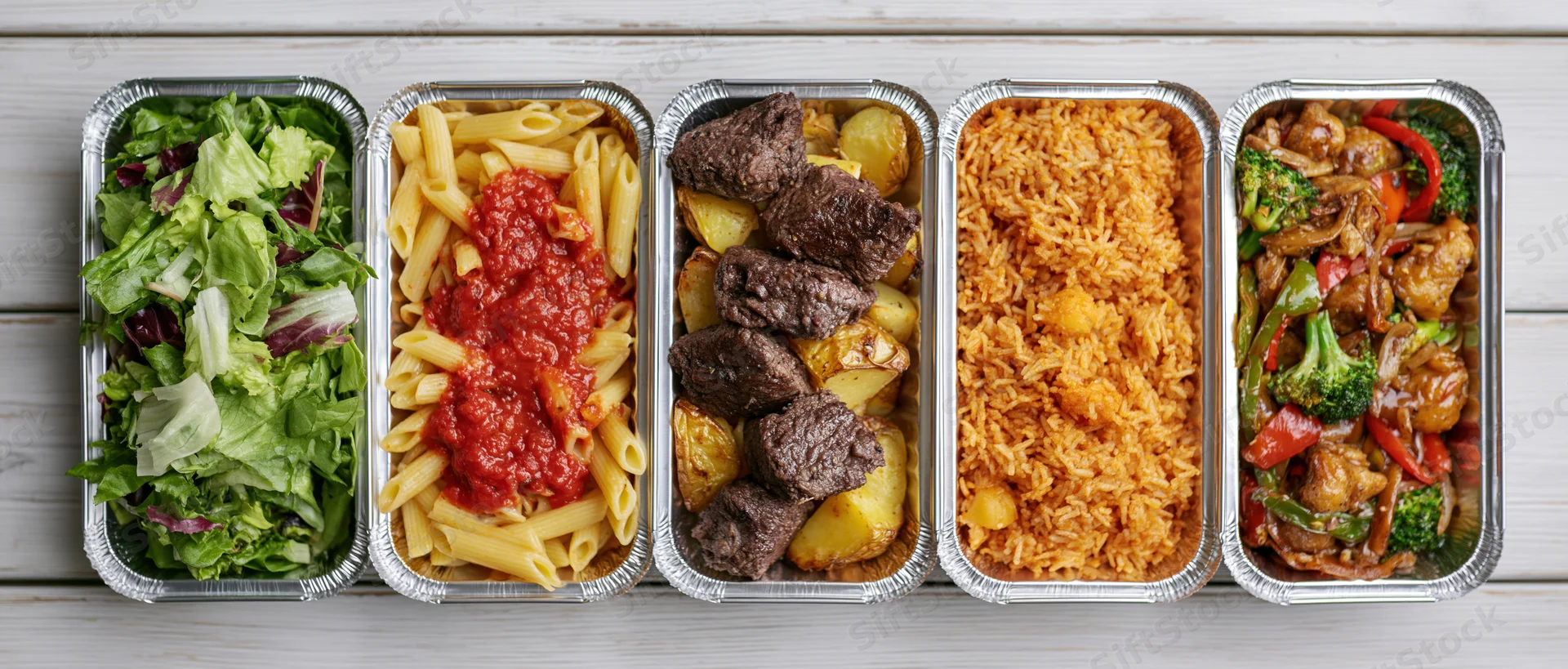 Five aluminum takeout containers in a row each filled with different meals including salad, pasta, beef with potatoes, rice, and stir-fry vegetables