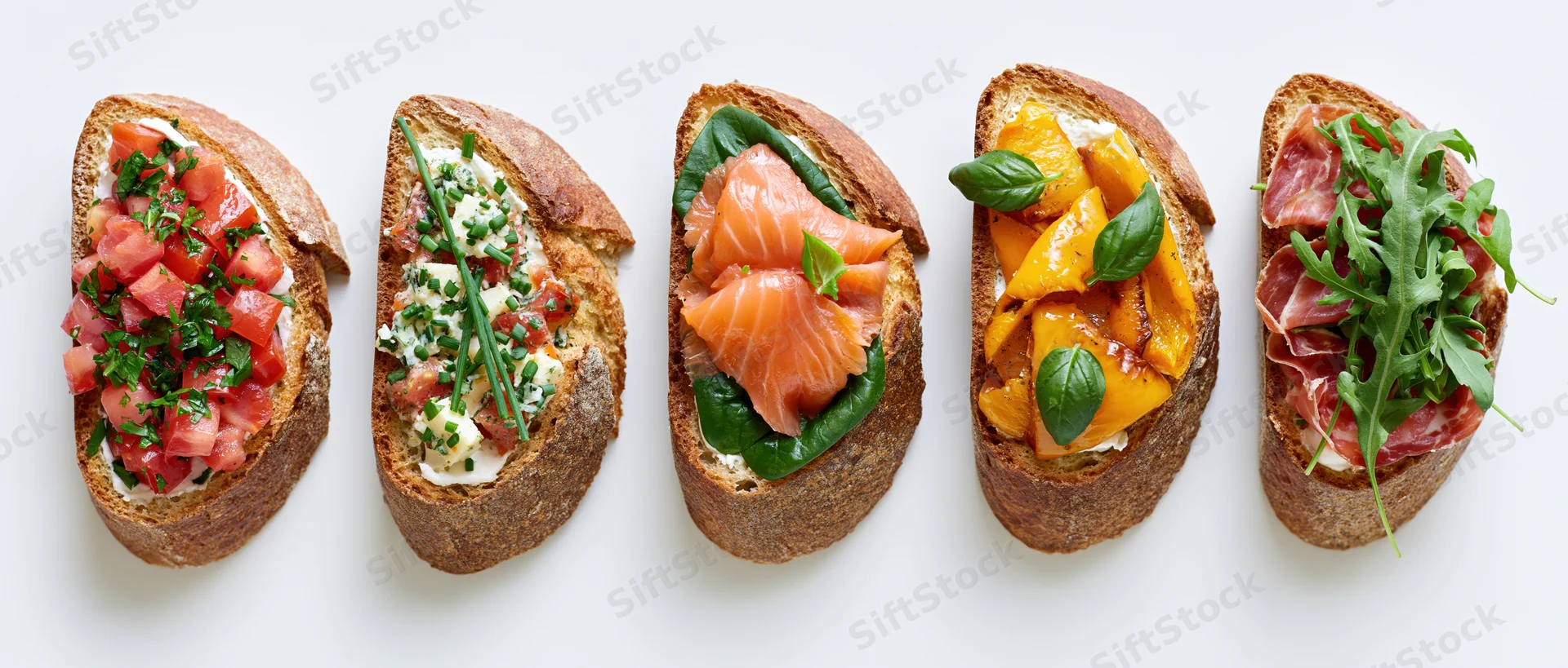 Five assorted bruschetta toasts arranged in a row on a white surface