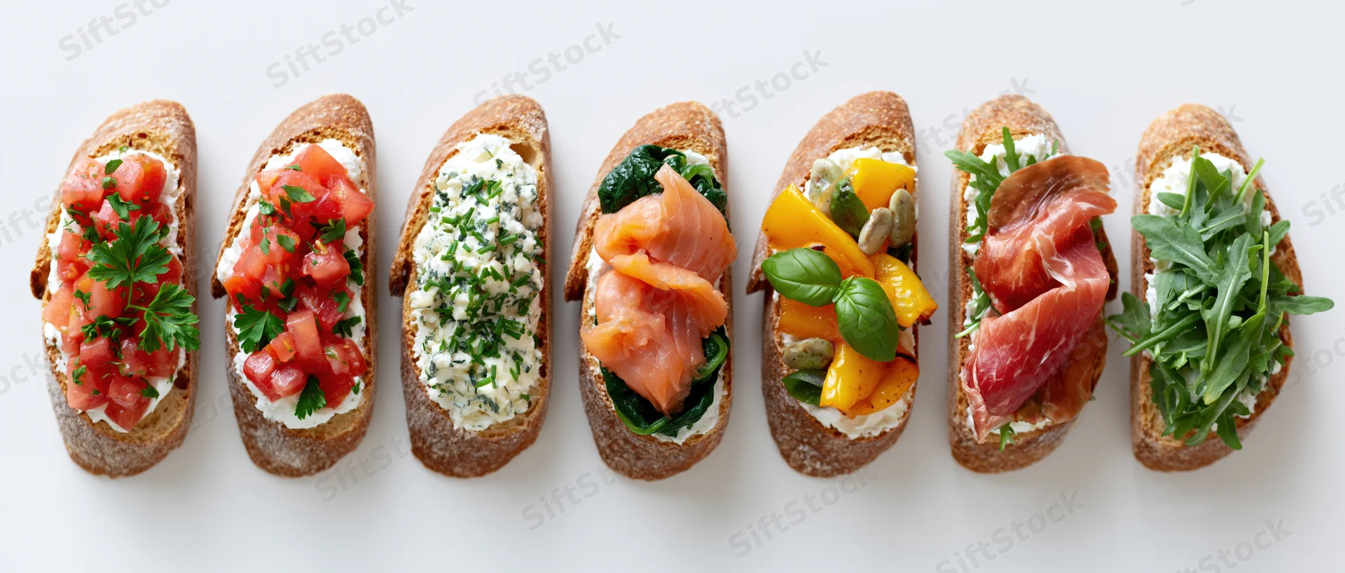 Seven bruschetta toasts with various toppings arranged in a row on a white surface