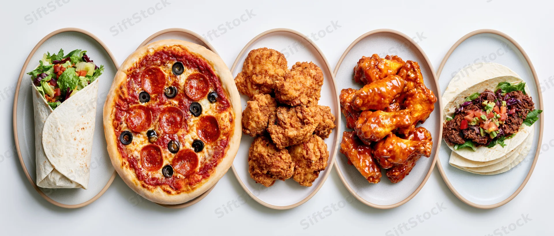 Five ceramic plates in a row each holding a different fast food dish viewed from above