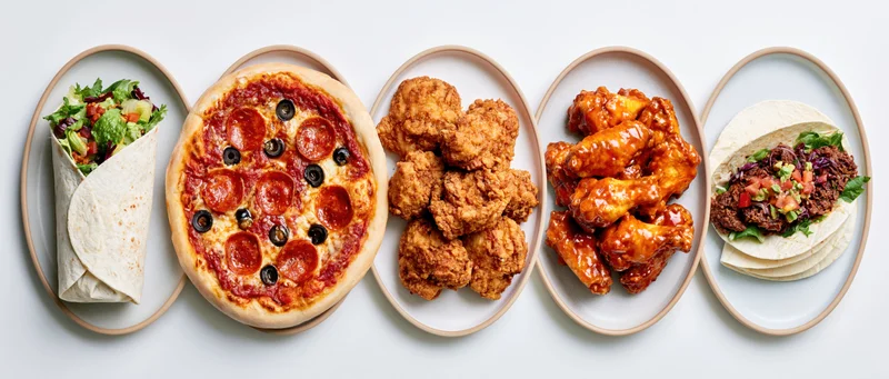 Five ceramic plates in a row each holding a different fast food dish viewed from above