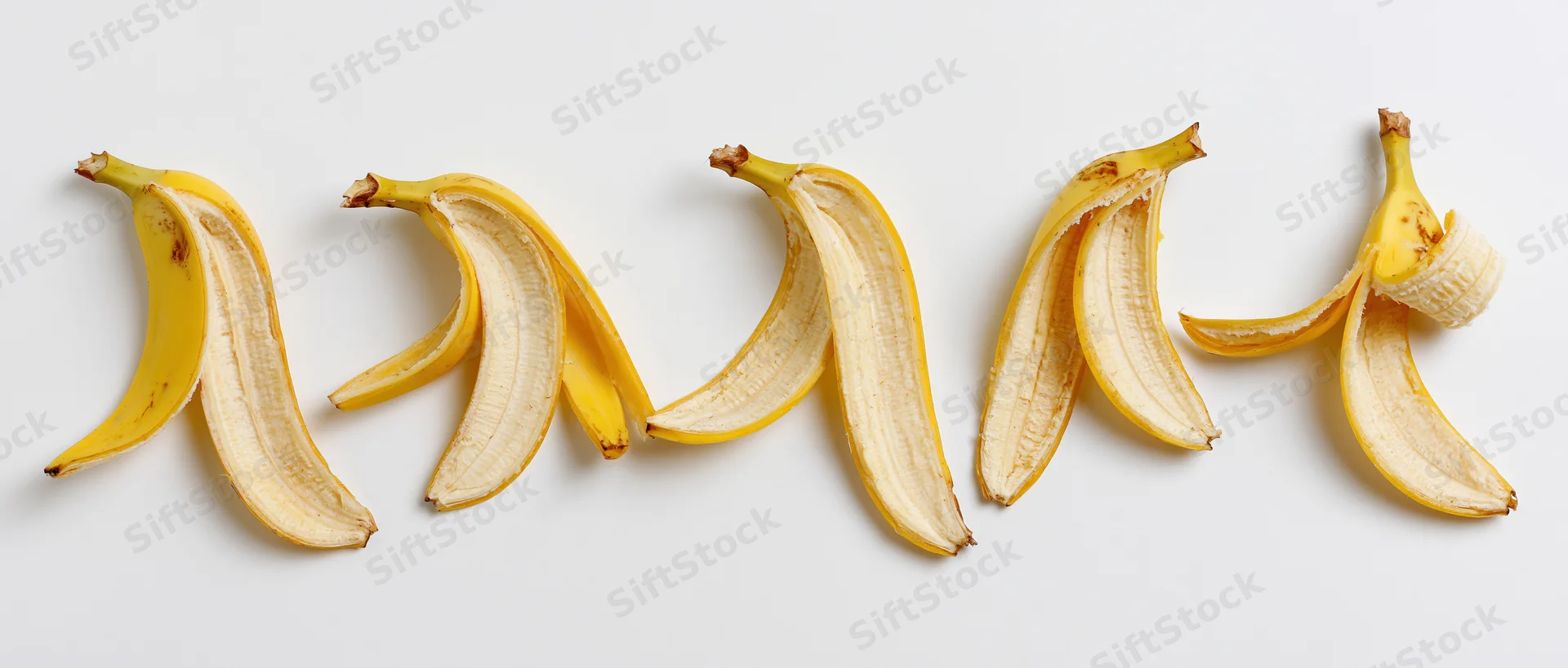 Five banana peels arranged in a horizontal row on a white surface