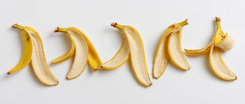 Five banana peels arranged in a horizontal row on a white surface