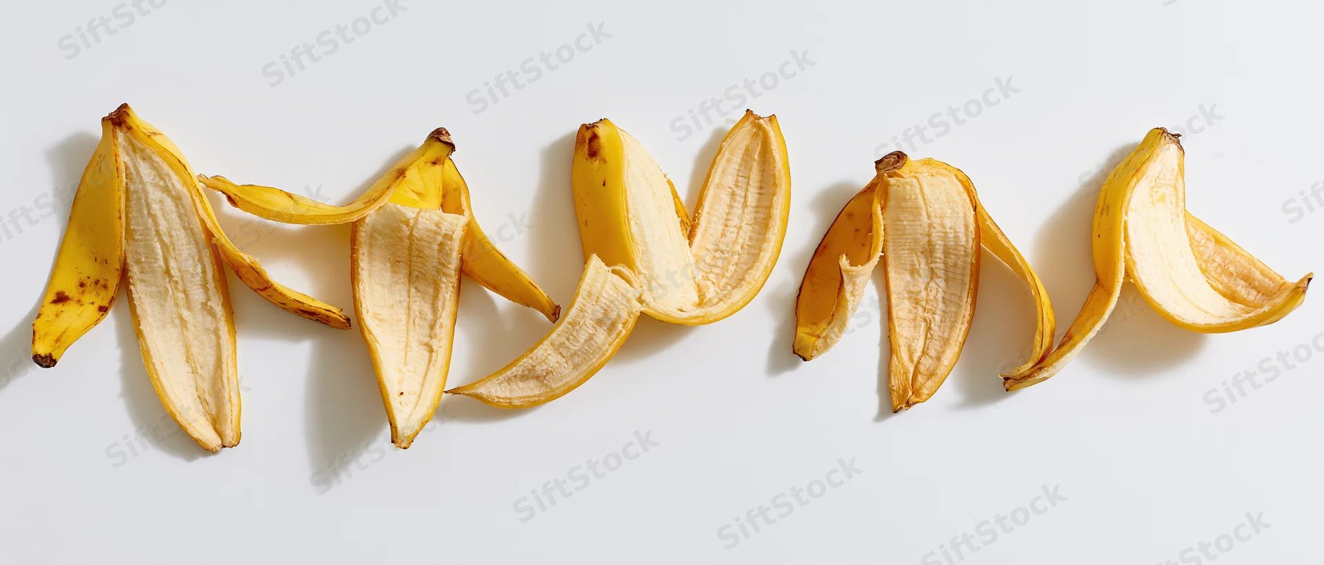 Five banana peels arranged in a horizontal row on a white surface