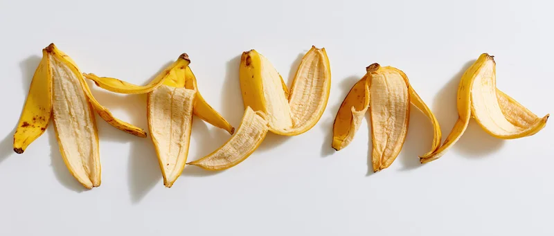 Five banana peels arranged in a horizontal row on a white surface