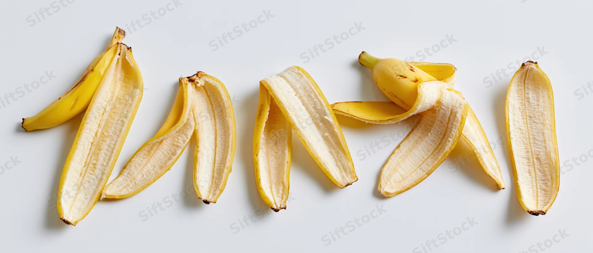 Five banana peels arranged in a horizontal row on a white surface