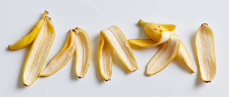 Five banana peels arranged in a horizontal row on a white surface