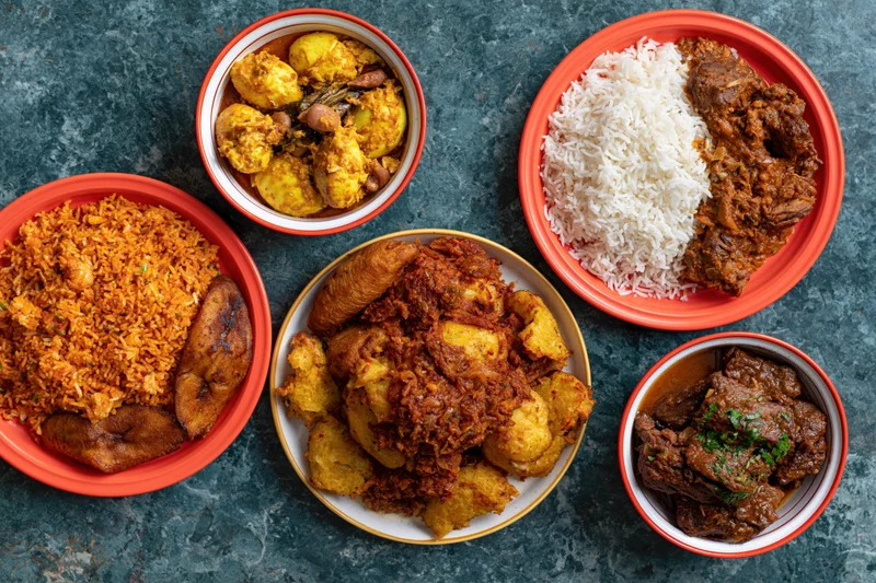 Five plates of west african food arranged on a dark teal stone surface