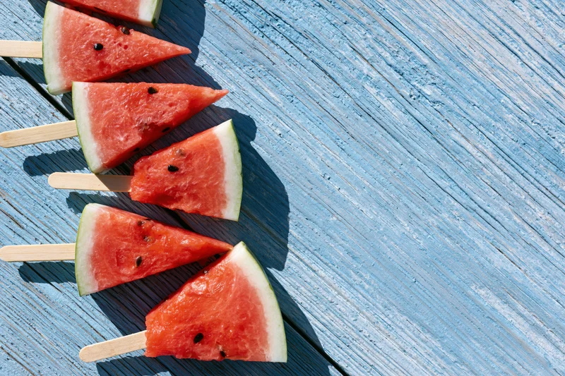 Watermelon slices on wooden sticks arranged diagonally on a blue weathered wood surface