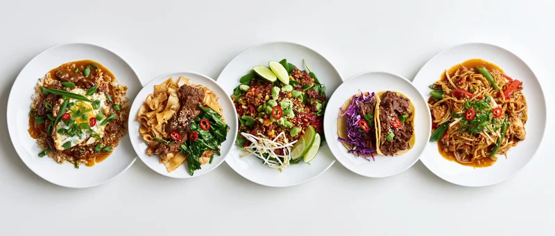 Five white plates of asian-inspired dishes arranged in a row on a white surface