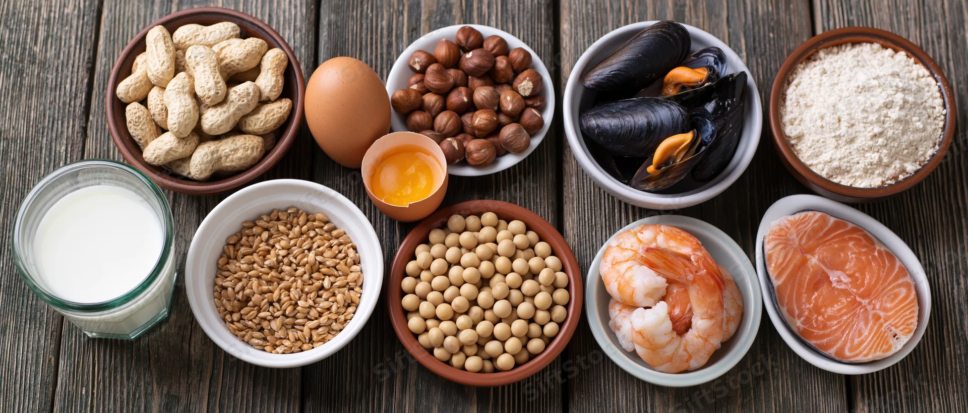 Common food allergens arranged in bowls and containers on a dark wooden surface