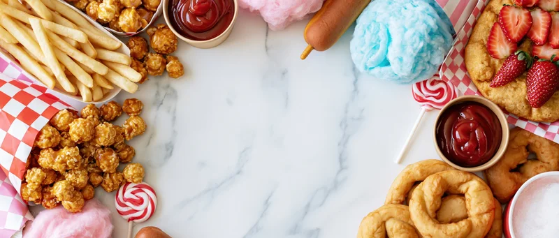 Carnival fair foods arranged in a border on a marble surface with copyspace in the center