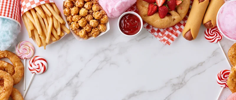 Carnival fair foods arranged in a border on a marble surface with copyspace in the center