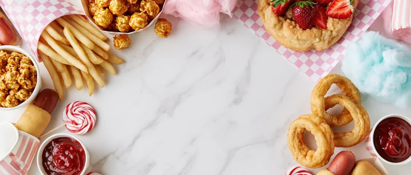 Carnival fair foods arranged in a border around a marble surface with copyspace in center