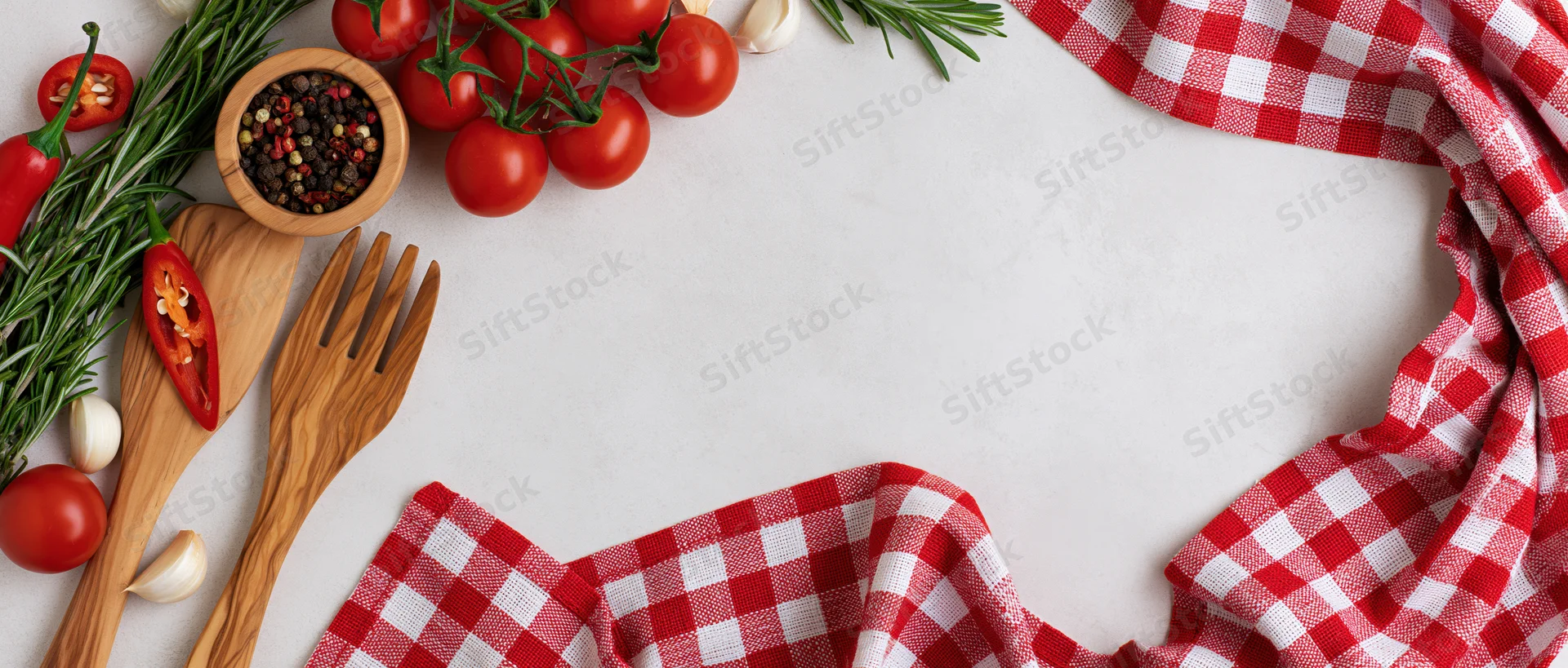 Fresh vegetables and wooden utensils arranged on a white surface with a red checkered cloth