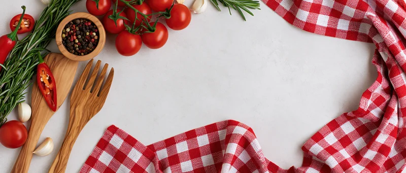 Fresh vegetables and wooden utensils arranged on a white surface with a red checkered cloth