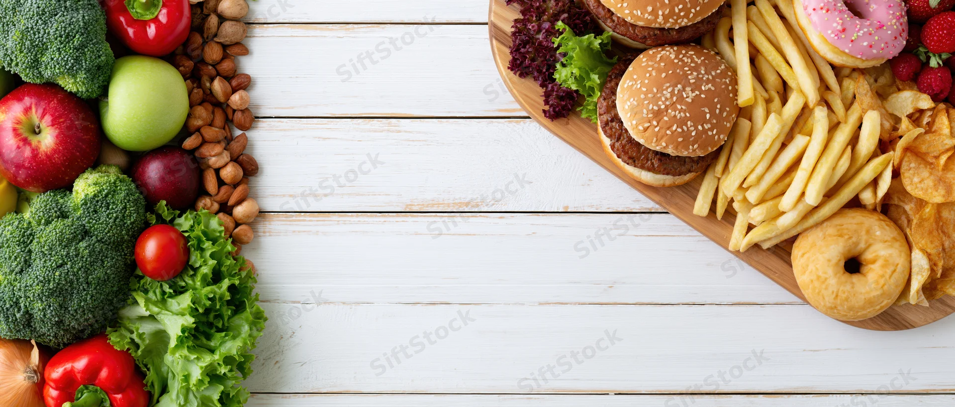 Healthy vegetables and fruits on one side, unhealthy fast food on the other, arranged on a white wooden table