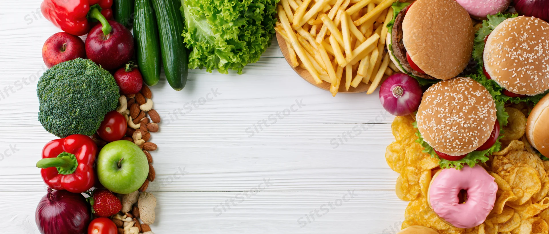 Healthy vegetables and fruits contrasted with unhealthy fast food on a white wooden table