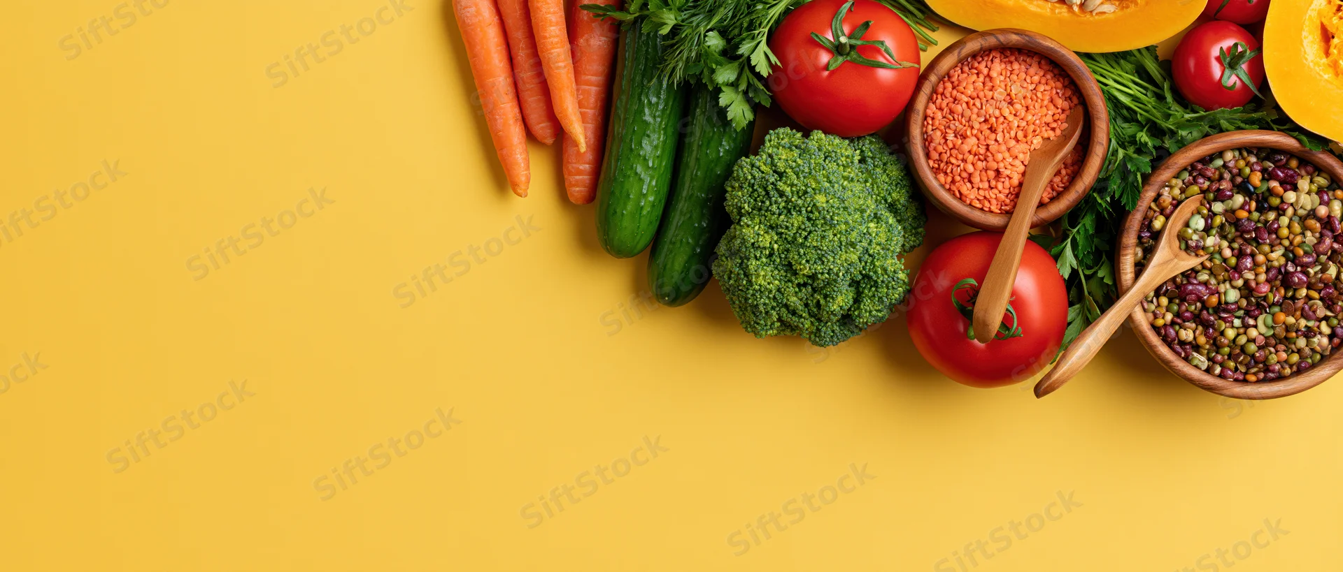 Fresh vegetables and legumes arranged in a flat lay on a yellow surface with copyspace
