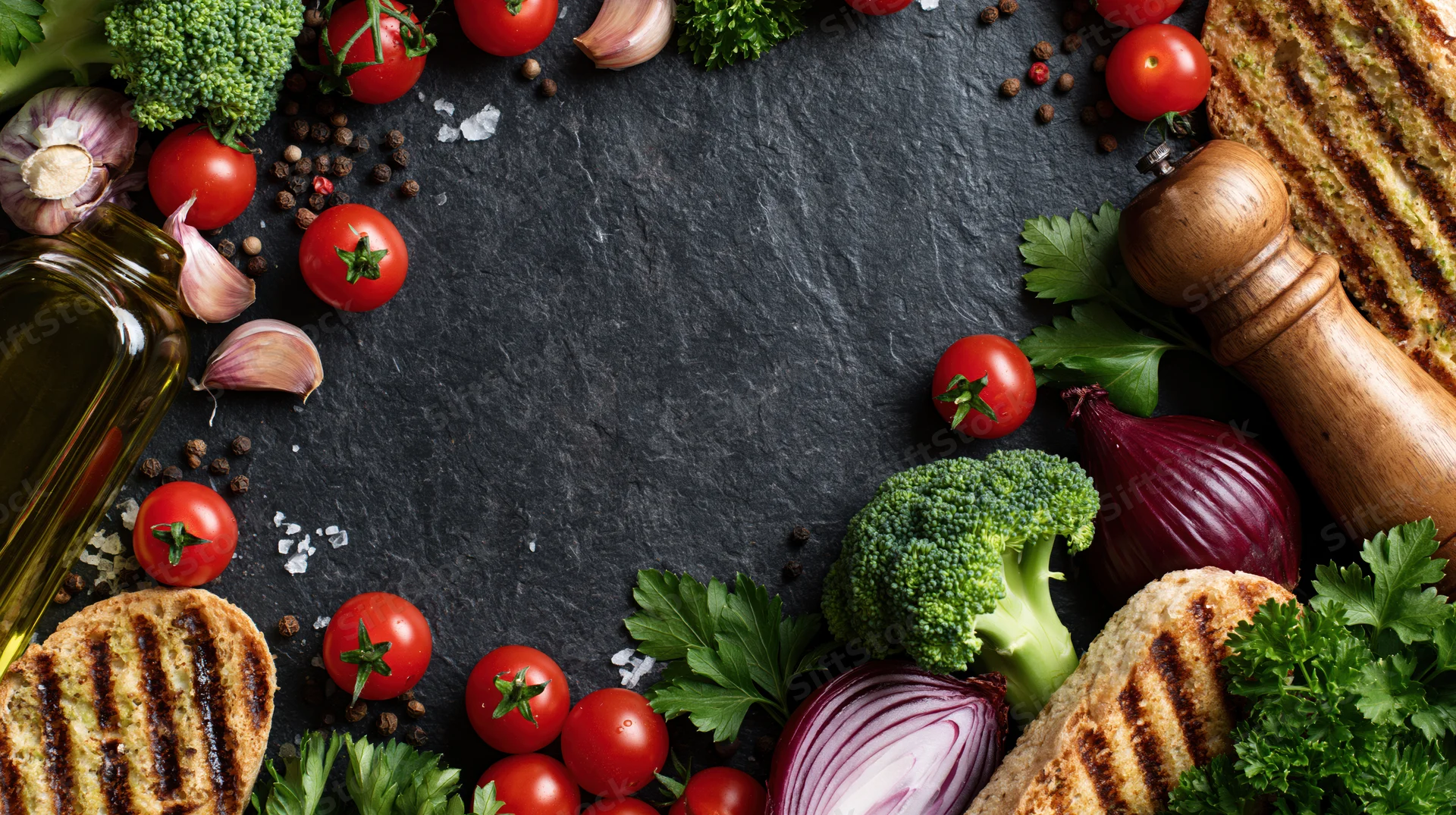 Fresh cooking ingredients arranged in a flat lay on dark slate surface with copyspace in center