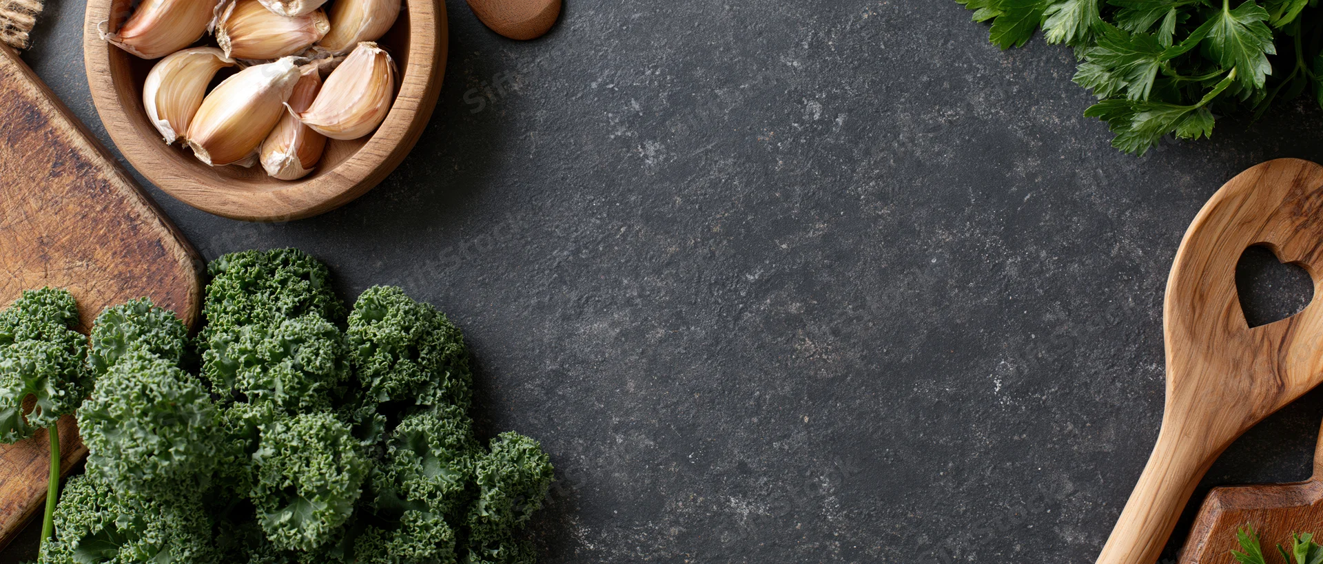 Kale and garlic arranged with wooden utensils and parsley on dark countertop