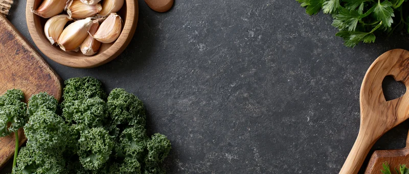 Kale and garlic arranged with wooden utensils and parsley on dark countertop