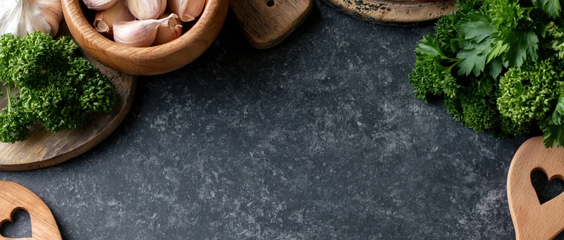 Fresh parsley and garlic arranged with wooden bowls and cutouts on a dark stone countertop