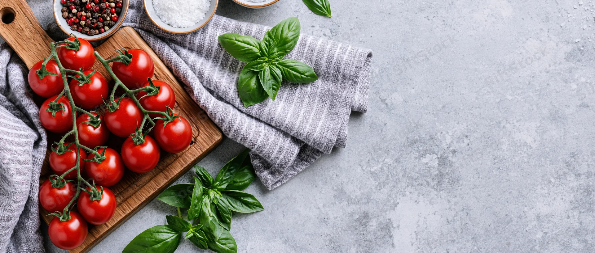 Vine cherry tomatoes on a wooden cutting board with basil and spices on a gray countertop