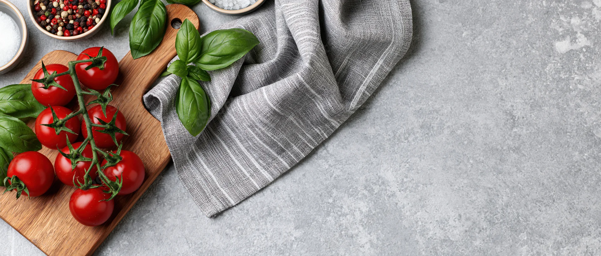 Vine tomatoes and basil on a wooden cutting board with striped cloth on gray countertop